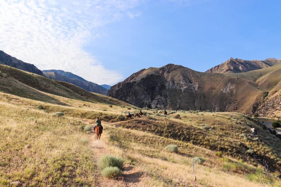 A hiker with a backpack descending a canyon trail alongside a river