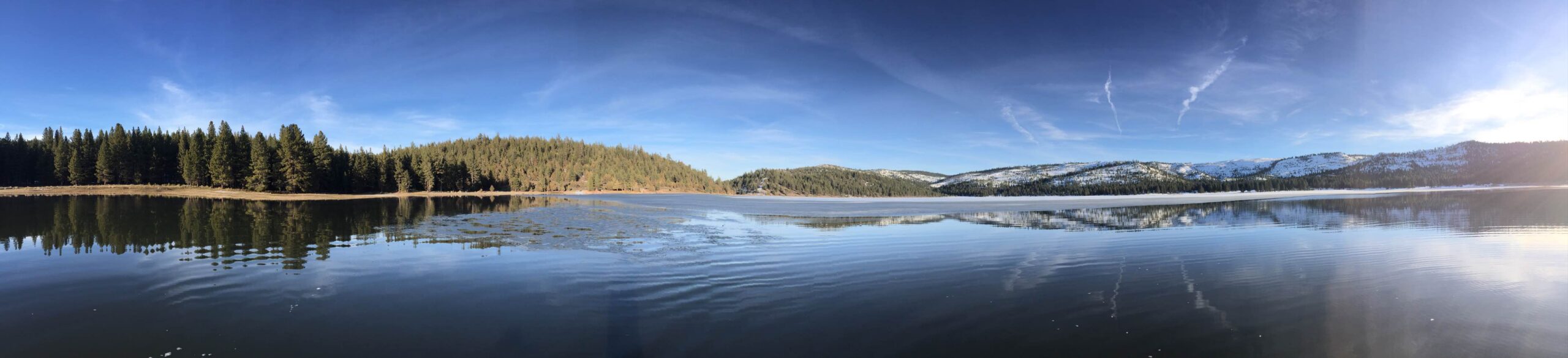 A wide panoramic view of Round Valley Reservoir with snow-dusted hills and calm reflective water