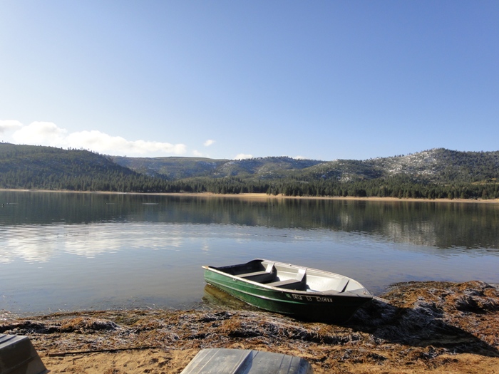 A green rowboat pulled up on the shoreline of Round Valley Reservoir with mountains reflected in the calm water